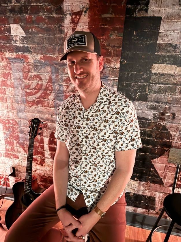 Weston Dean, smiling portrait against a painted brick wall